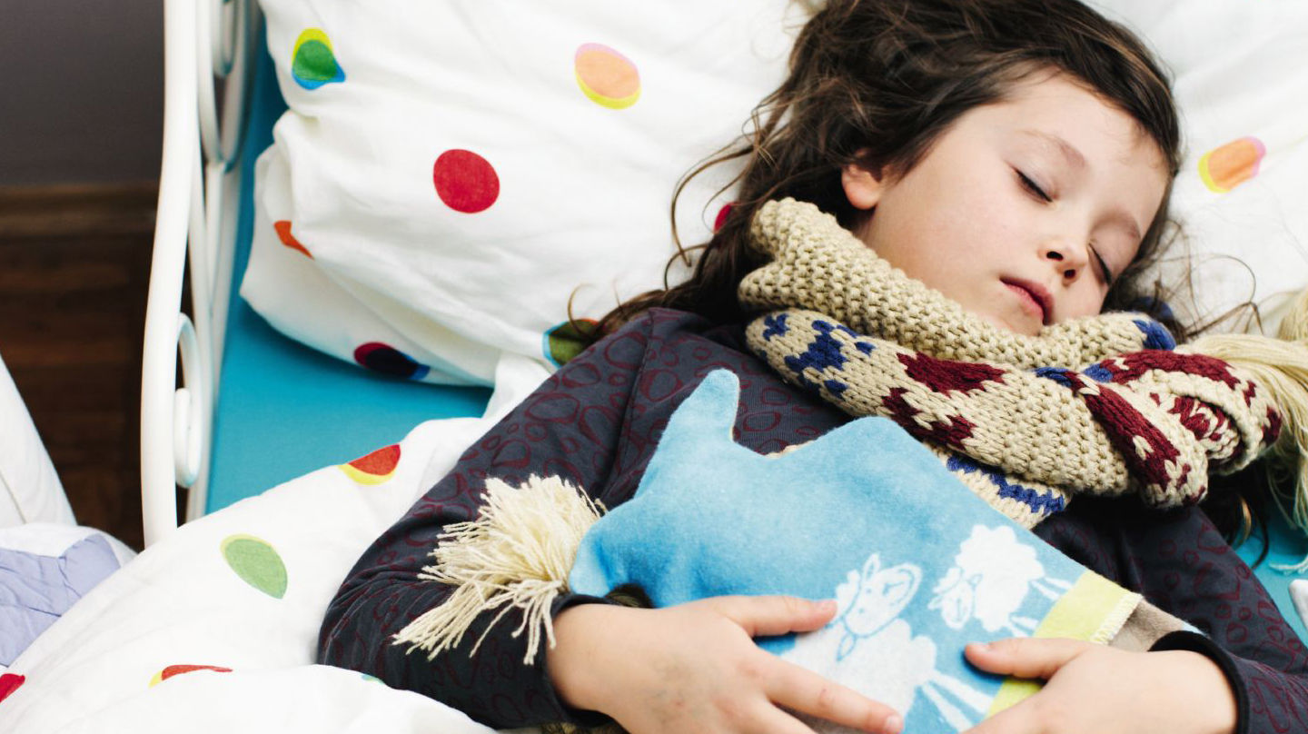 Erkältung bei Kindern: Mädchen mit Schal und Wärmflasche liegt schlafend im Bett